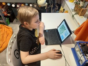 Uczeń siedzi przy biurku, gra zdalnie w szachy przez internet.