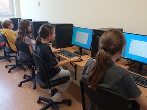 Uczniowie siedzą przy stanowiskach komputerowych.