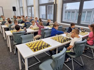 Szachiści uczestniczący w XXVI Otwartym Turnieju Szachowym Siedmiu Gwiazd siedzą przy stolikach i grają w szachy.