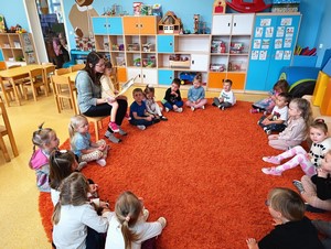Rodzic dziecka z oddziału przedszkolnego (4 - latki) czyta bajkę dzieciom siedzącym w kółku.