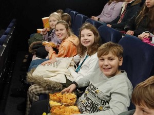 Uczniowie z klas 4 siedzą na fotelach w kinie przed seansem filmowym.