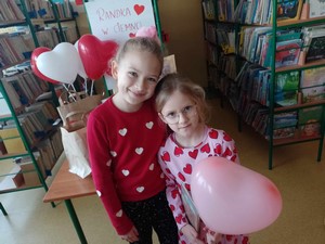 Dwie uczennice prezentują się do zdjęcia w Bibliotece Szkolnej trzymając balonik.