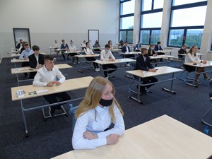 Uczniowie siedzą przy ławeczkach na auli i piszą egzamin ósmoklasisty.