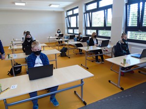 Uczniowie siedzą przy stolikach z komputerami i rozwiązują konkurs multimedialny.