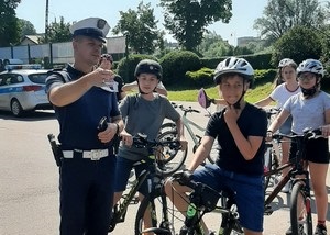 Uczniowie na rowerach słuchają policjanta, który omawia trasę egzaminacyjną.