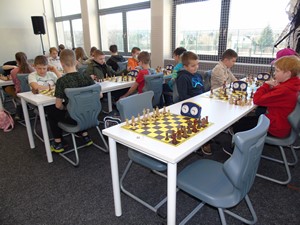 Szachiści siedzą przy stolikach i grają w szachy.