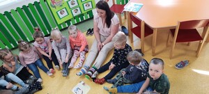 Dzieci z oddziału przedszkolnego (3 - latki) wraz z wychowawczynią siedzą na podłodze i prezentują kolorowe skarpetki.