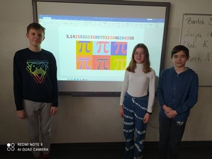 Trójka uczniów stoi przy tablicy z wyświetloną liczbą PI.