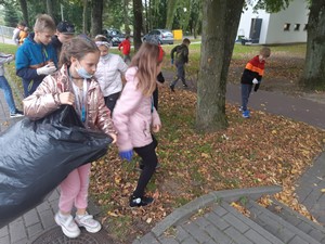 Uczniowie z workami na chodniku przed szkołą sprzątają świat.
