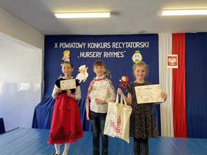 Trójka uczniów, którzy wzięli udział w X Powiatowym Konkursie Recytatorskim "Nursery Rhymes" prezentuje się do zdjęcia trzymając dyplomy i nagrody.