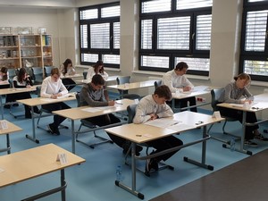 Uczniowie klas 8 siedzą przy stolikach i piszę próbny egzamin ósmoklasisty.