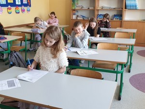 Uczniowie klas 3 siedzą w ławeczkach i rozwiązują Test Umiejętności Trzecioklasisty.