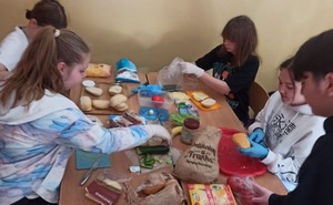 Uczniowie - wolontariusze siedzą przy stoliku i wykonują kanapki.