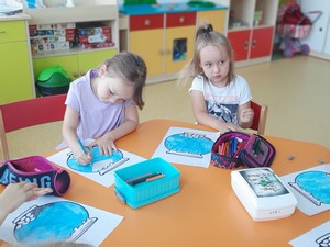 Dzieci z oddziałów przedszkolnych siedzą przy stoliku i rysują prace plastyczne.