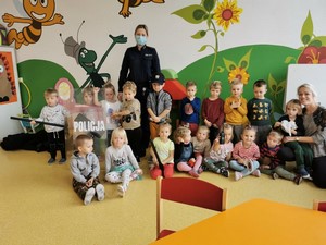 Dzieci z oddziału przedszkolnego (3 - latki) wraz z wychowawczynią i p. policjantką prezentują się do zdjęcia.