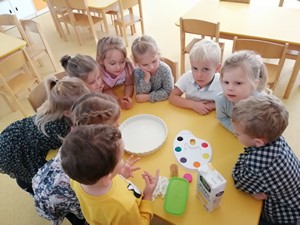Dzieci z oddziału przedszkolnego (4 - latki) siedzą przy stoliku z przyborami do malowania na mleku.