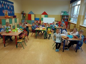 Uczniowie z oddziału przedszkolnego 01 siedzą przy stolikach o prezentują się do zdjęcia.