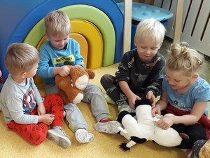 Dzieci z oddziałów przedszkolnych (4 latki) siedzą na podłodze i opatrują pluszakom sztuczne rany.