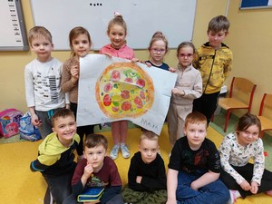 Dzieci z oddziału przedszkolnego (4 latki) prezentują się do zdjęcia z plakatem przedstawiającym pizzę.