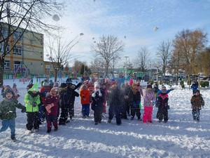 Dzieci z zerówek bawią się przed szkołą na śniegu.