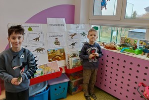 Dwójka dzieci z oddziału przedszkolnego 5-latków prezentuje się do zdjęcia przy gazetce nt. dinozaurów.