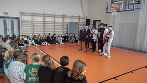 Chłopcy z Samorządu Uczniowskiego na sali gimnastycznej grają na gitarach piosenki przed dziewczętami.