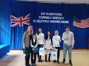 Uczniowie szkoły, którzy wzięlli udział w konkursie języka angielskiego wraz z opiekunką prezentują się do zdjęcia na okazjonalnej gazetce.