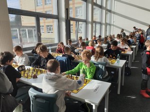 Szachiści siedzą przy stolikach na sali gimnastycznej i grają w szachy.