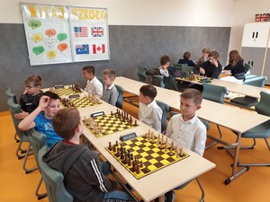 Dzieci biorący udział w gminnych eliminacjach 51 Igrzysk Dzieci i Młodzieży Szkolnej w Szachach Drużynowych siedzą przy stolikach z szachami.