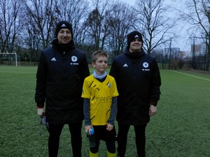 Konrad Reszka prezentuje się do zdjęcia wraz z dwoma trenerami piłkarskimi.