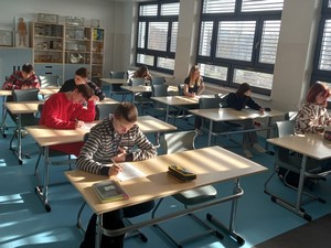 Uczniowie biorący udział w etapie szkolnym XIII Powiatowego Konkursu "ABC Młodego Ekonomisty" siedzą przy stolikach i rozwiązują test.