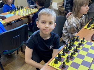 Uczeń - szachista siedzi przy stoliku z szachownicą.