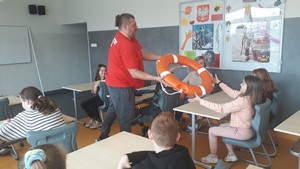 Ratownik podaje koło ratunkowe uczniowi podczas warsztatów dla uczniów z klas 3 "Bezpieczne wakacje nad wodą".
