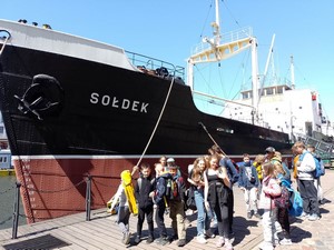Grupa uczniów prezentuje się do zdjęcia przed statkiem Sołdek.