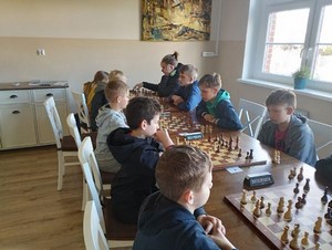 Szachiści siedzą przy stolikach w sali i grają w szachy.