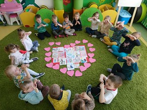 Dzieci z oddziału przedszkolnego (3 - latki) siedzą na dywanie wokół serca w którym znajdują się rysunki z dobrymi uczynkami.