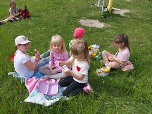 Dzieci z oddziału przedszkolnego (6 - latki) siedzą na trawniku podczas pikniku.