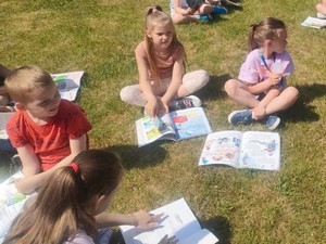 Dzieci czytają książki na trawniku przed szkołą.