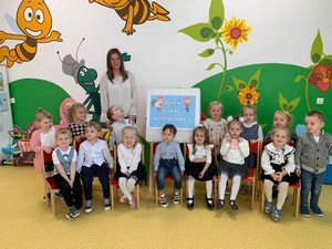 Dzieci z oddziałów przedszkolnych (3 latki) wraz z wychowawczynią prezentują się do zdjęcia na tle napisu "Dzień Edukacji Narodowej".