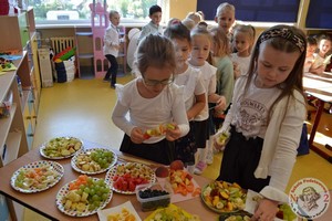 Dzieci z oddziałów przedszkolnych (zerówka) przygotowują owocowe szaszłyki przy stoliku.