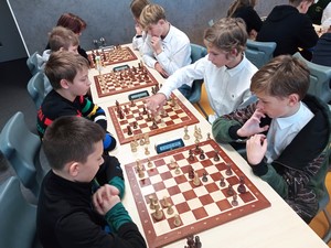 Uczniowie siedzą przy stolikach i grają w szachy.