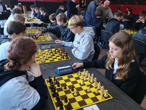 Uczniowie siedzą przy stolikach i grają w szachy.