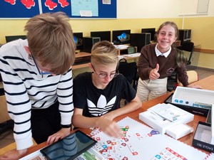 Uczniowie z klasy 7 siedzą przy stole i programują za pomocą gry Scottie Go!