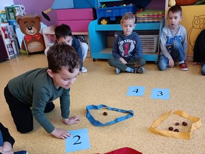 Dzieci z oddziałów przedszkolnych (5 latki) siedzą na podłodze i rozwiązują zadania matematyczne.