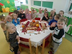 Dzieci z oddziałów przedszkolnych (3 latki) stoją wokół stołu, na którym ustawione są różne chleby.