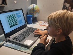 Uczeń siedzi przed komputerem i uczestniczy w internetowym turnieju szachowym.