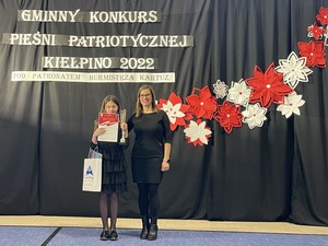 Uczennica Alicja Marszk wraz z nauczycielką muzyki prezentują się do zdjęcia podczas V Gminnego Konkursu Pieśni Patriotycznej w Kiełpinie.