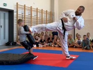 Trener karate podczas pokazu kopie osłonę, którą trzyma uczeń.