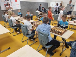 Uczestnicy gminnych eliminacji Igrzysk Dzieci i Młodzieży w Szachach Drużynowych grają przy stolikach w szachy.