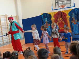 Dzieci z oddziału przedszkolnego (4 - latki) stoją na scenie wraz z aktorem podczas spektaklu "Rubinowy Książe" na sali gimnastycznej.